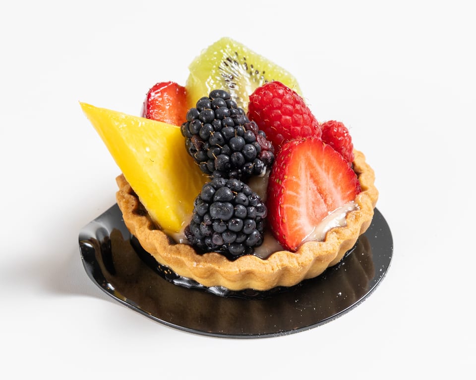 A vibrant fruit tart with mango, kiwi, blackberries, raspberries, and strawberries on a black plate.