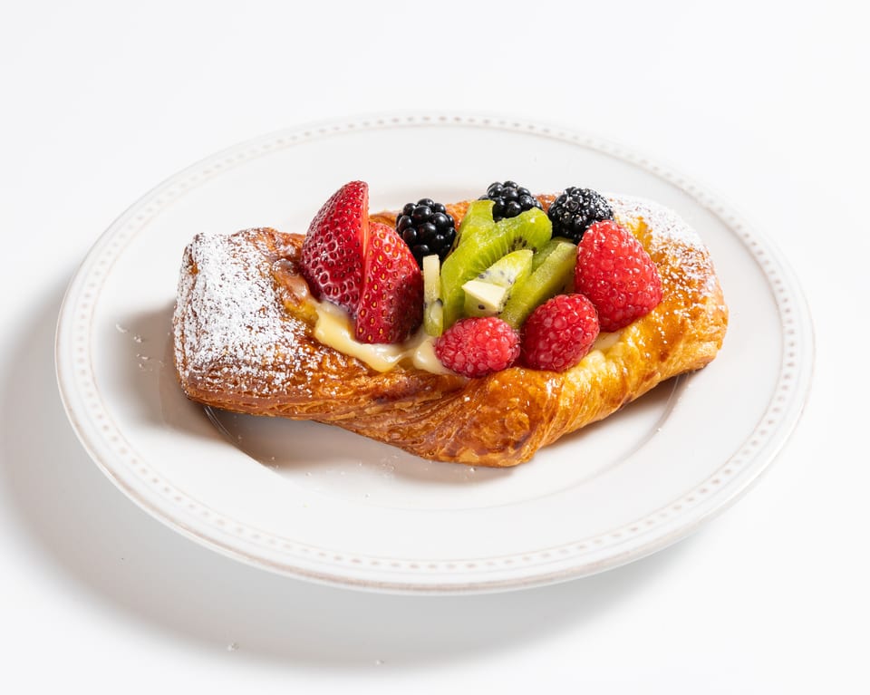 A golden-brown fruit pastry with custard, strawberries, raspberries, blackberries, and kiwi, dusted with powdered sugar.