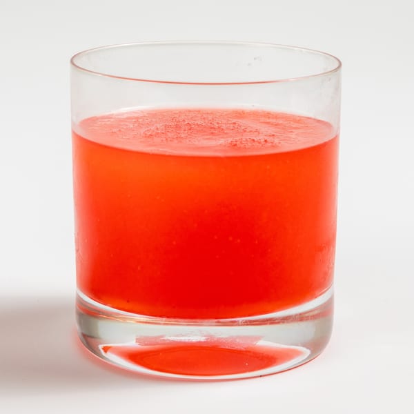 A clear glass filled with a vibrant red beverage, possibly a cocktail or juice, on a white background.