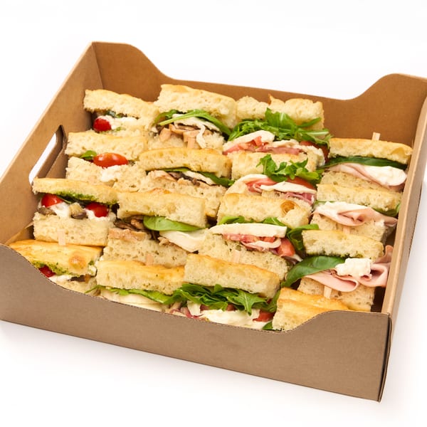A brown cardboard box filled with many small focaccia sandwiches with various fillings.