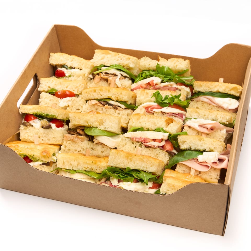 A brown cardboard box filled with many small focaccia sandwiches with various fillings.