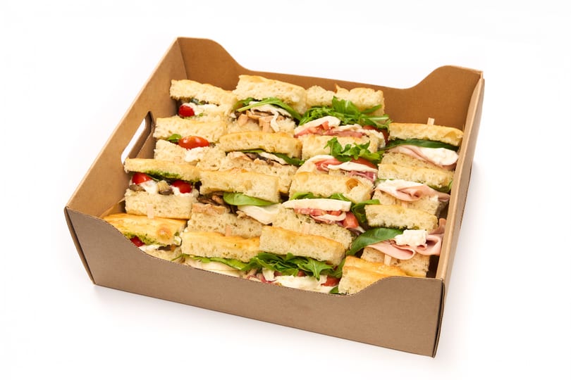 A brown cardboard box filled with many small focaccia sandwiches with various fillings.
