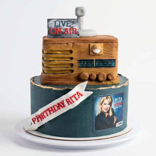 Two-tier cake with a vintage radio on top, "LIVE ON AIR" sign, and "BIRTHDAY RITA" banner.