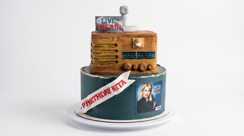 Two-tier cake with a vintage radio on top, "LIVE ON AIR" sign, and "BIRTHDAY RITA" banner.