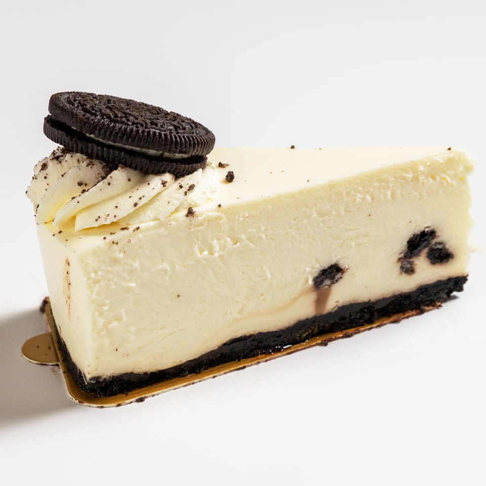 A slice of cookies and cream cheesecake with an Oreo cookie on top, on a white background.