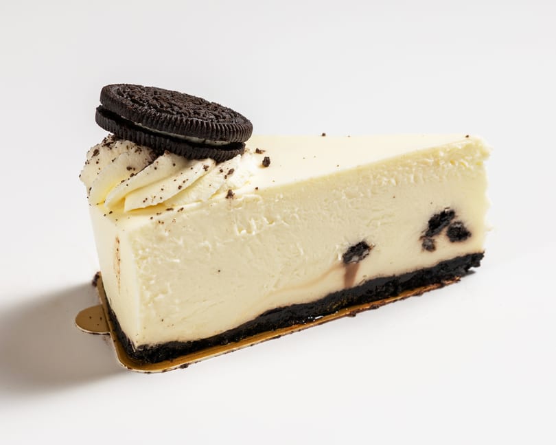 A slice of cookies and cream cheesecake with an Oreo cookie on top, on a white background.