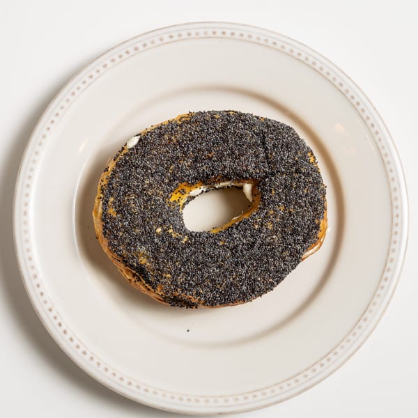 Poppy seed bagel with cream cheese on a white plate, viewed from above.