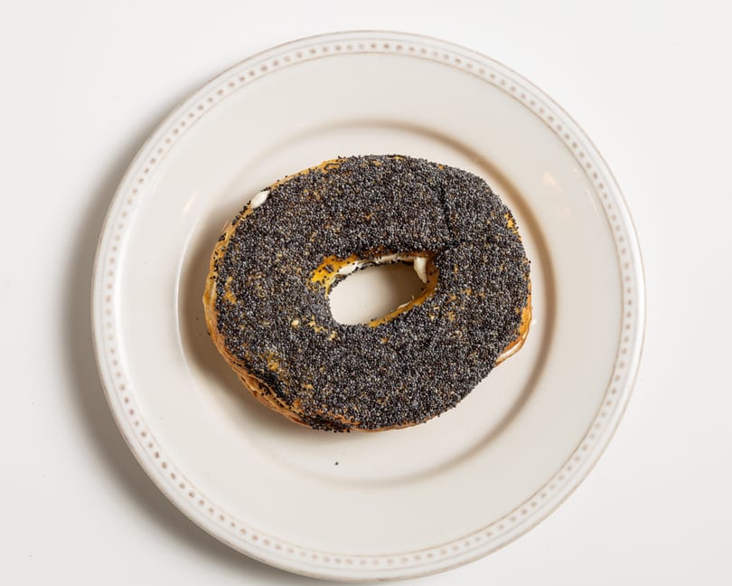 Poppy seed bagel with cream cheese on a white plate, viewed from above.