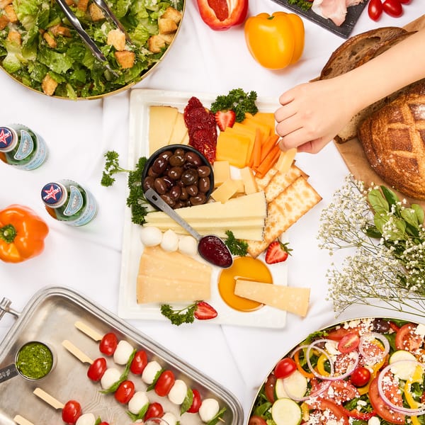 Overhead view of a buffet spread with salads, charcuterie, cheese board, and caprese skewers.