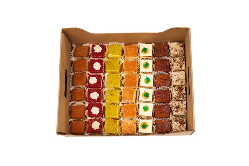 A catering box of assorted mini cakes and petit fours in a rainbow of colors and flavors.
