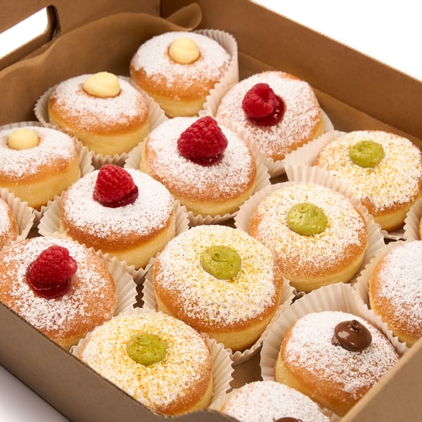 A box of powdered sugar donuts with various toppings including raspberries, yellow cream, and green cream.