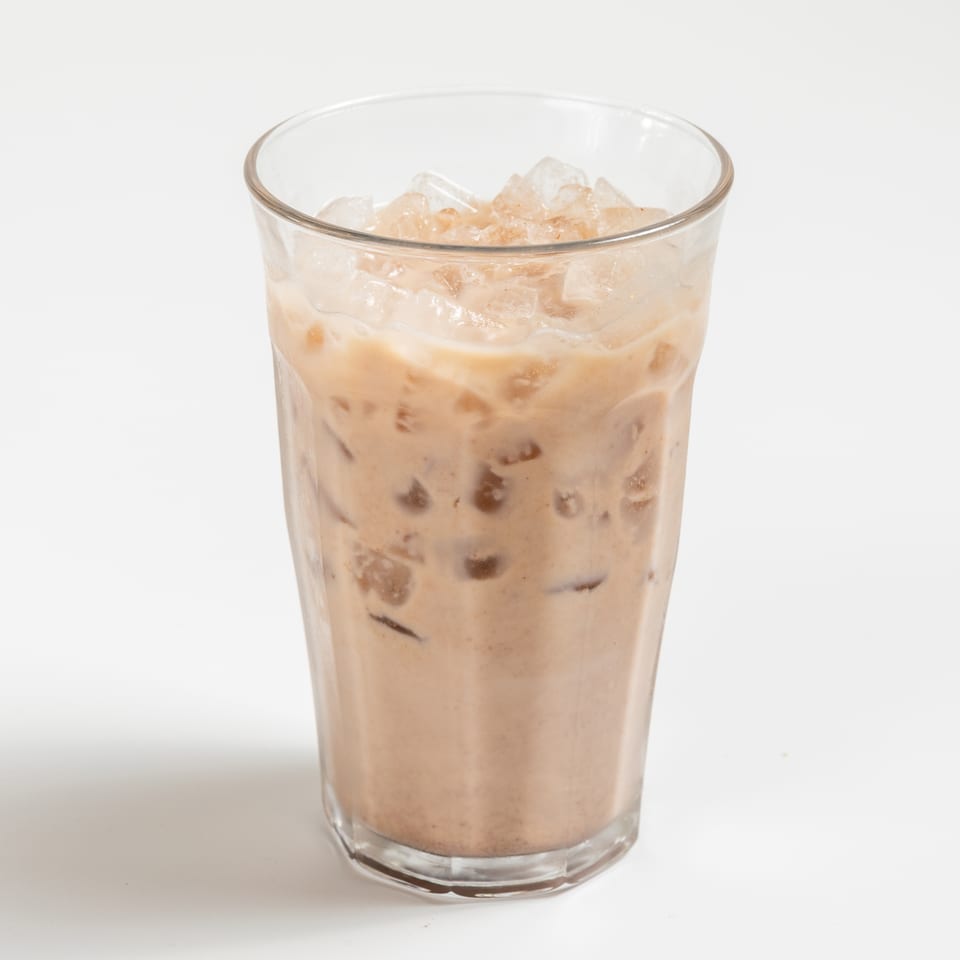 Iced coffee with milk and ice cubes in a clear glass on a white background.