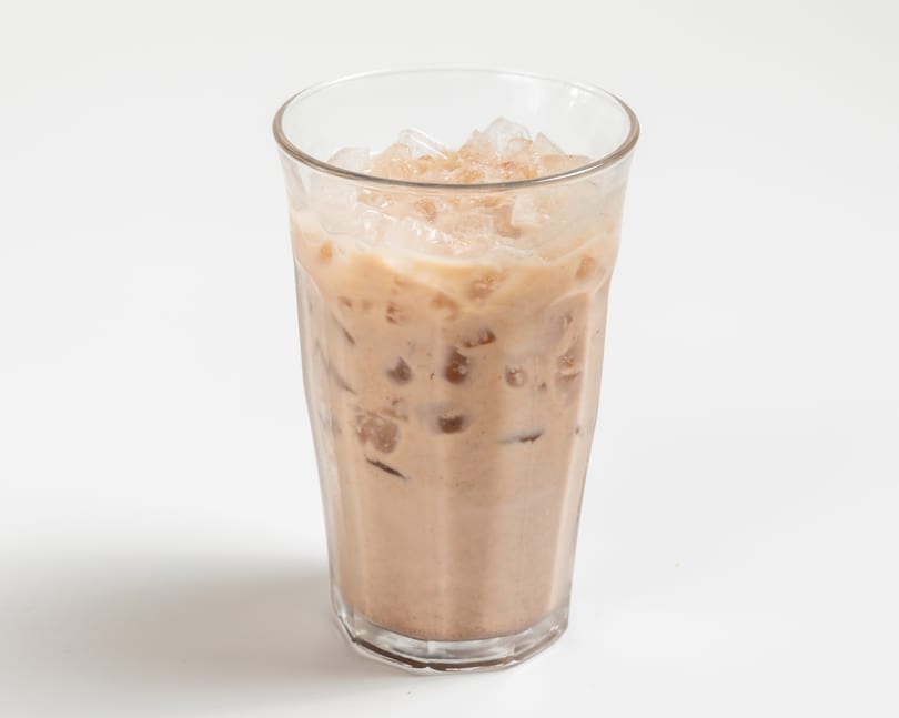 Iced coffee with milk and ice cubes in a clear glass on a white background.