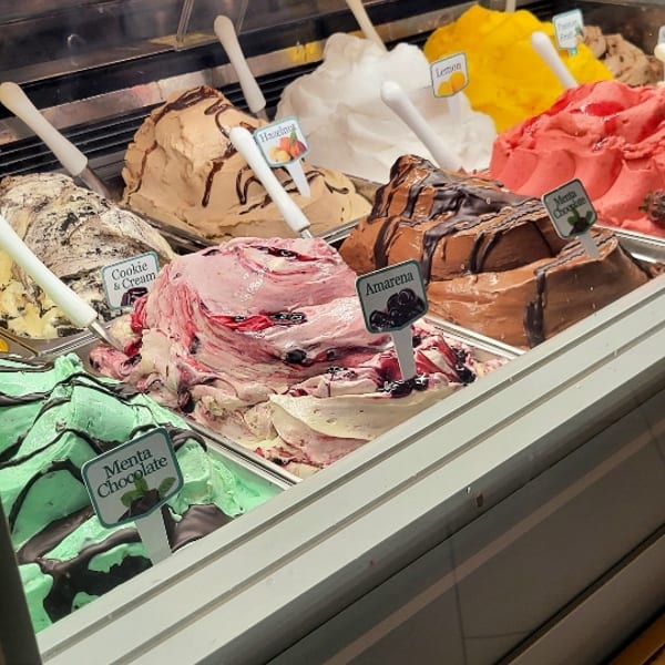 A gelato display case filled with colorful flavors including Menta Chocolate, Cookie & Cream, Amarena, and Hazelnut.
