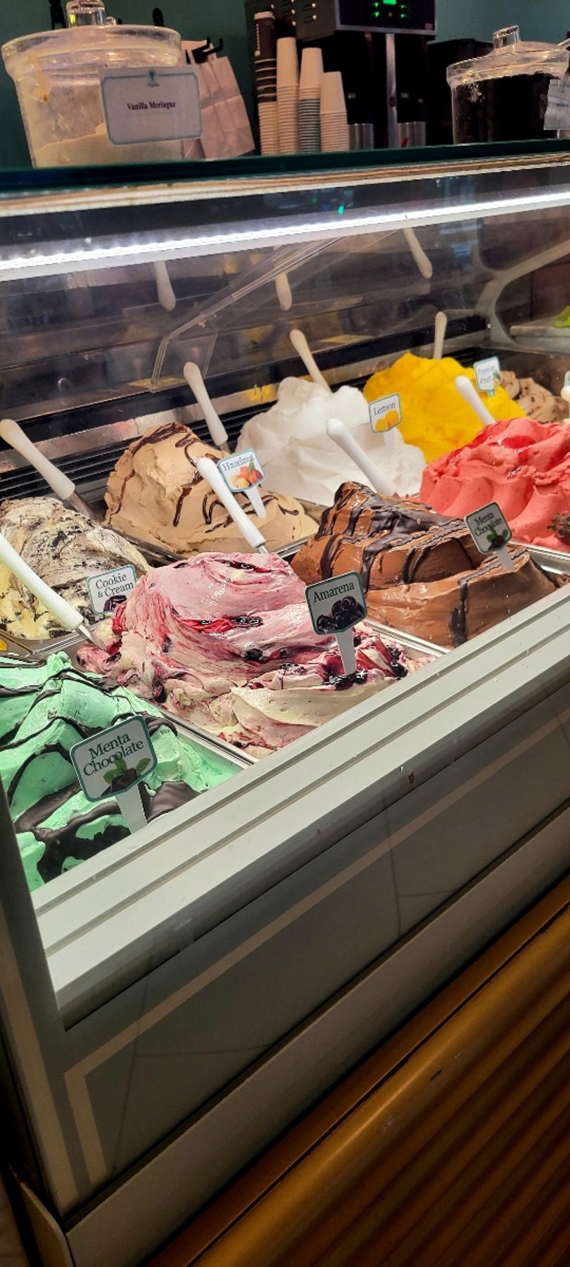 A gelato display case filled with colorful flavors including Menta Chocolate, Cookie & Cream, Amarena, and Hazelnut.