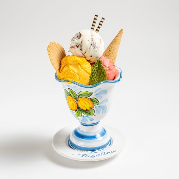 Colorful scoops of gelato in a decorative cup with waffle cookies, chocolate sticks, and mint.