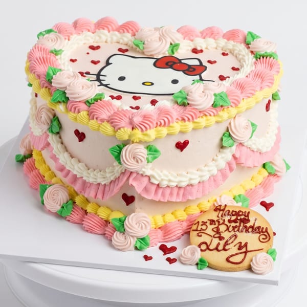 Heart-shaped Hello Kitty cake with pink, yellow, and white frosting, roses, and red hearts.