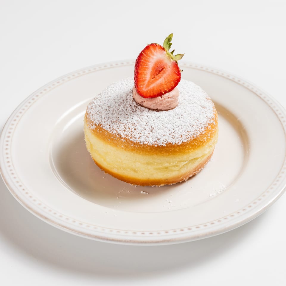 Powdered sugar donut with strawberry cream and a fresh strawberry half on a white plate.