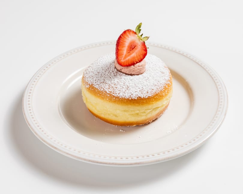 Powdered sugar donut with strawberry cream and a fresh strawberry half on a white plate.