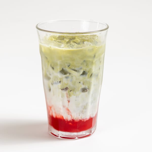 A vibrant layered drink with red strawberry syrup, white milk, and green matcha tea over ice.