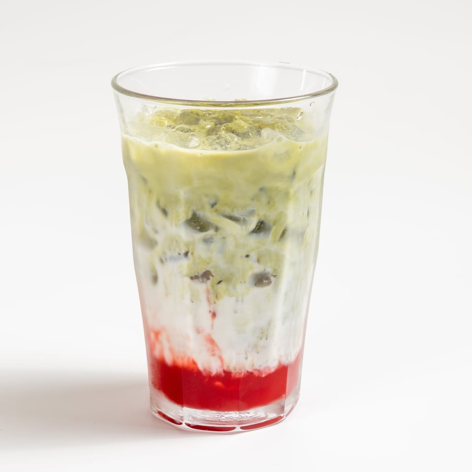 A vibrant layered drink with red strawberry syrup, white milk, and green matcha tea over ice.