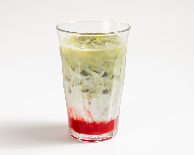 A vibrant layered drink with red strawberry syrup, white milk, and green matcha tea over ice.
