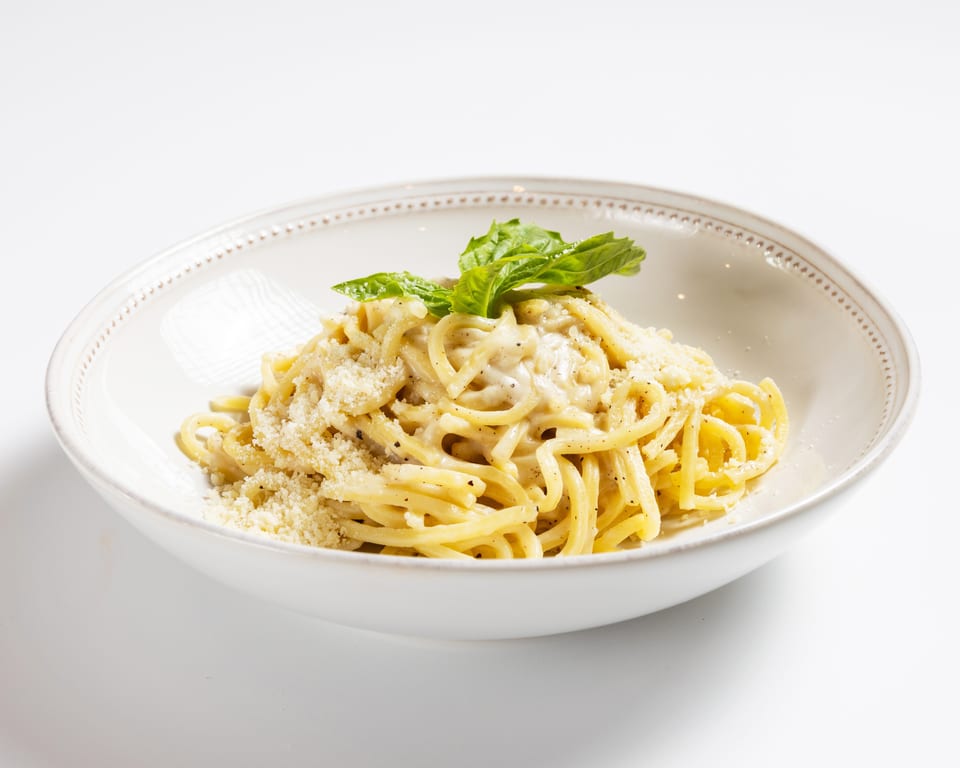 Creamy spaghetti carbonara with grated cheese and fresh basil in a white bowl.