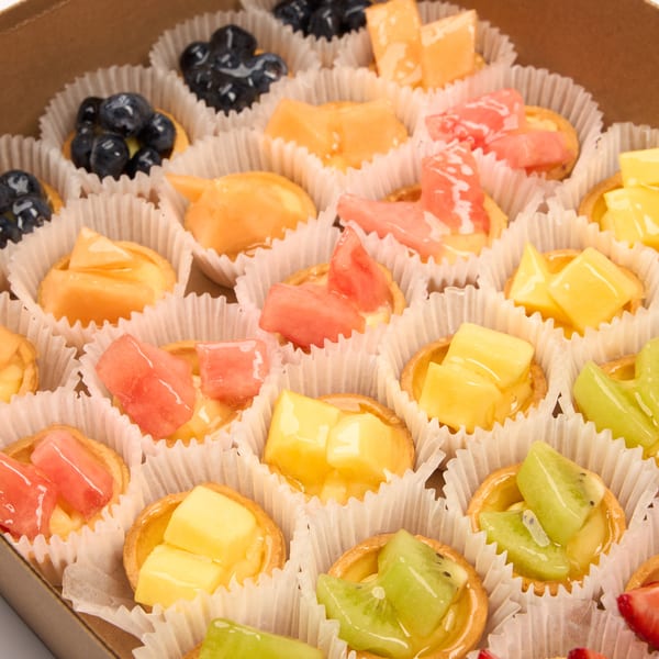 A cardboard box filled with rows of mini fruit tarts, each in a white paper cup.