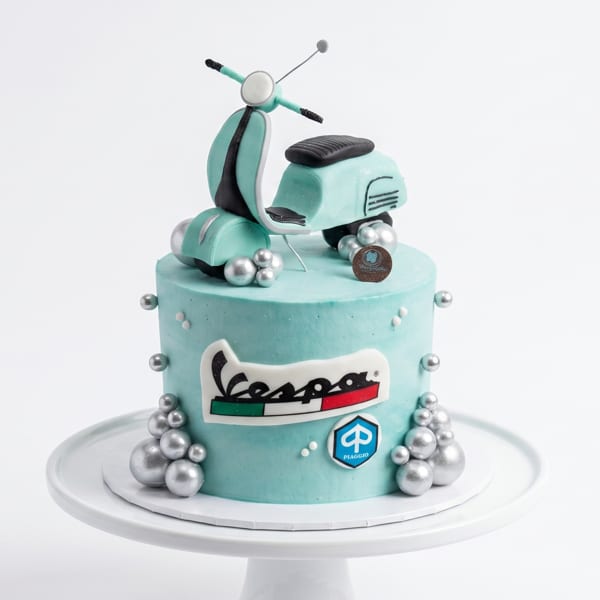 A light blue Vespa-themed cake with a miniature scooter on top and silver edible pearls.