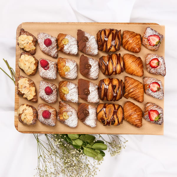 Assortment of croissants with various toppings like almonds, raspberries, chocolate, and strawberries on a wooden board.