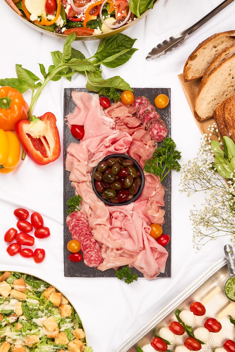 Overhead view of a buffet spread with charcuterie, salads, bread, and Caprese skewers.