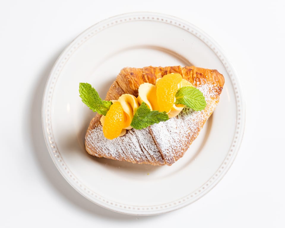 Croissant dusted with powdered sugar, topped with orange segments, banana slices, and mint leaves.