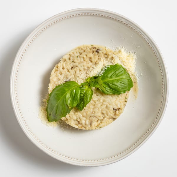 Creamy mushroom risotto topped with grated Parmesan cheese and fresh basil leaves in a white bowl.