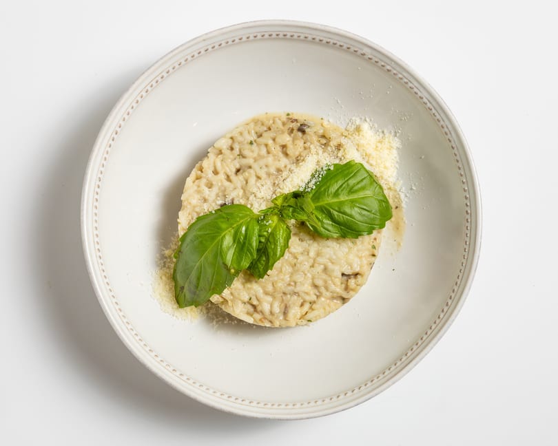 Creamy mushroom risotto topped with grated Parmesan cheese and fresh basil leaves in a white bowl.