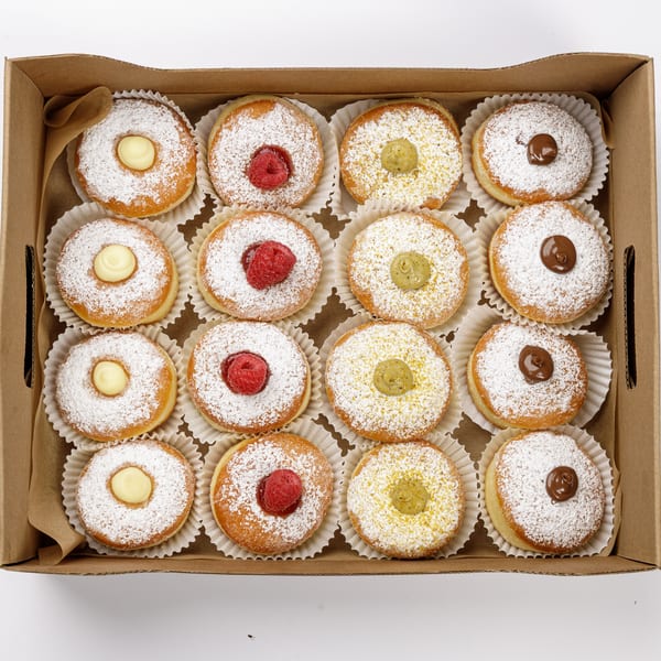 A box of mini bomboloni donuts dusted with powdered sugar and filled with cream, raspberry, pistachio, and chocolate.