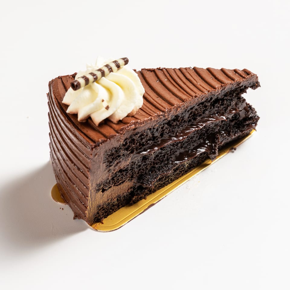 A rich chocolate cake slice with whipped cream and a chocolate stick on a white background.