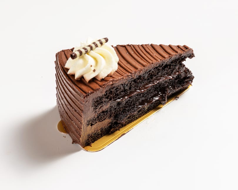 A rich chocolate cake slice with whipped cream and a chocolate stick on a white background.