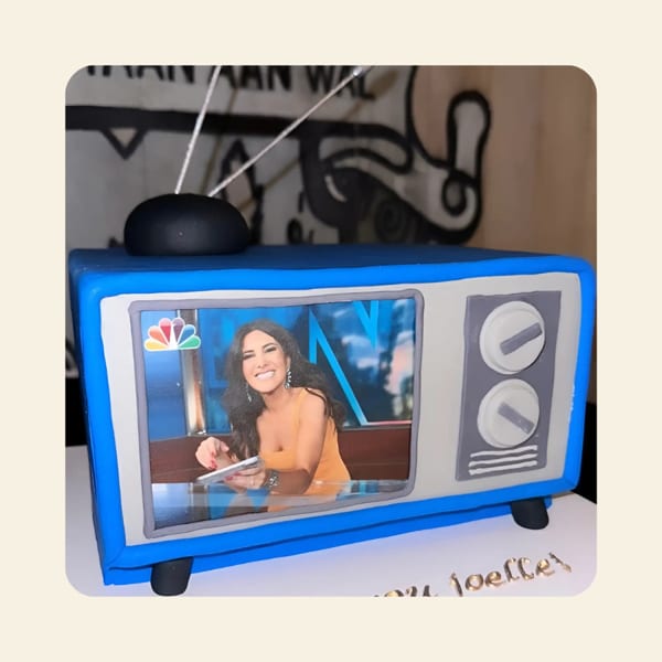 A blue and gray retro TV-shaped cake with a smiling woman on the screen.