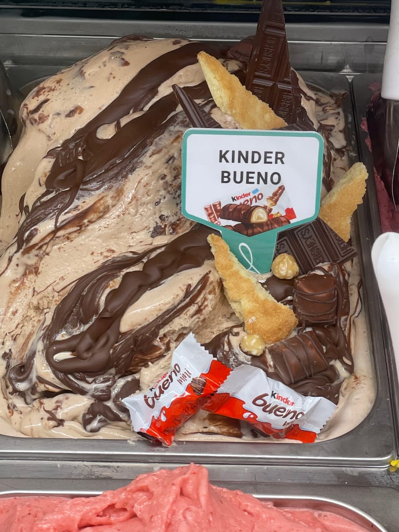 Kinder Bueno gelato topped with chocolate drizzle, sponge, chocolate bars, and Kinder Bueno candies.