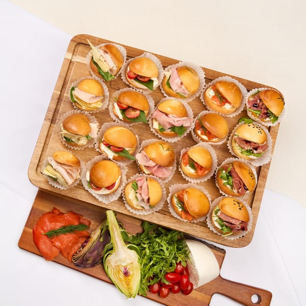 Assortment of mini sandwiches on wooden boards with fresh ingredients like salmon, artichoke, and mozzarella.