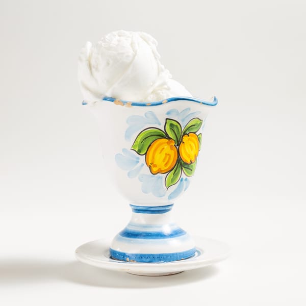 White ice cream in a decorative ceramic cup with painted lemons and blue stripes.