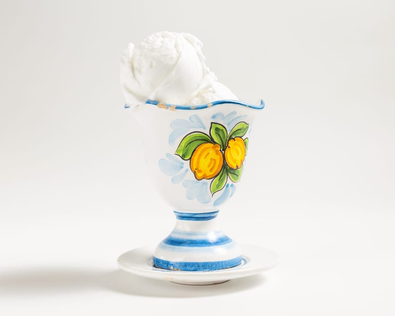 White ice cream in a decorative ceramic cup with painted lemons and blue stripes.