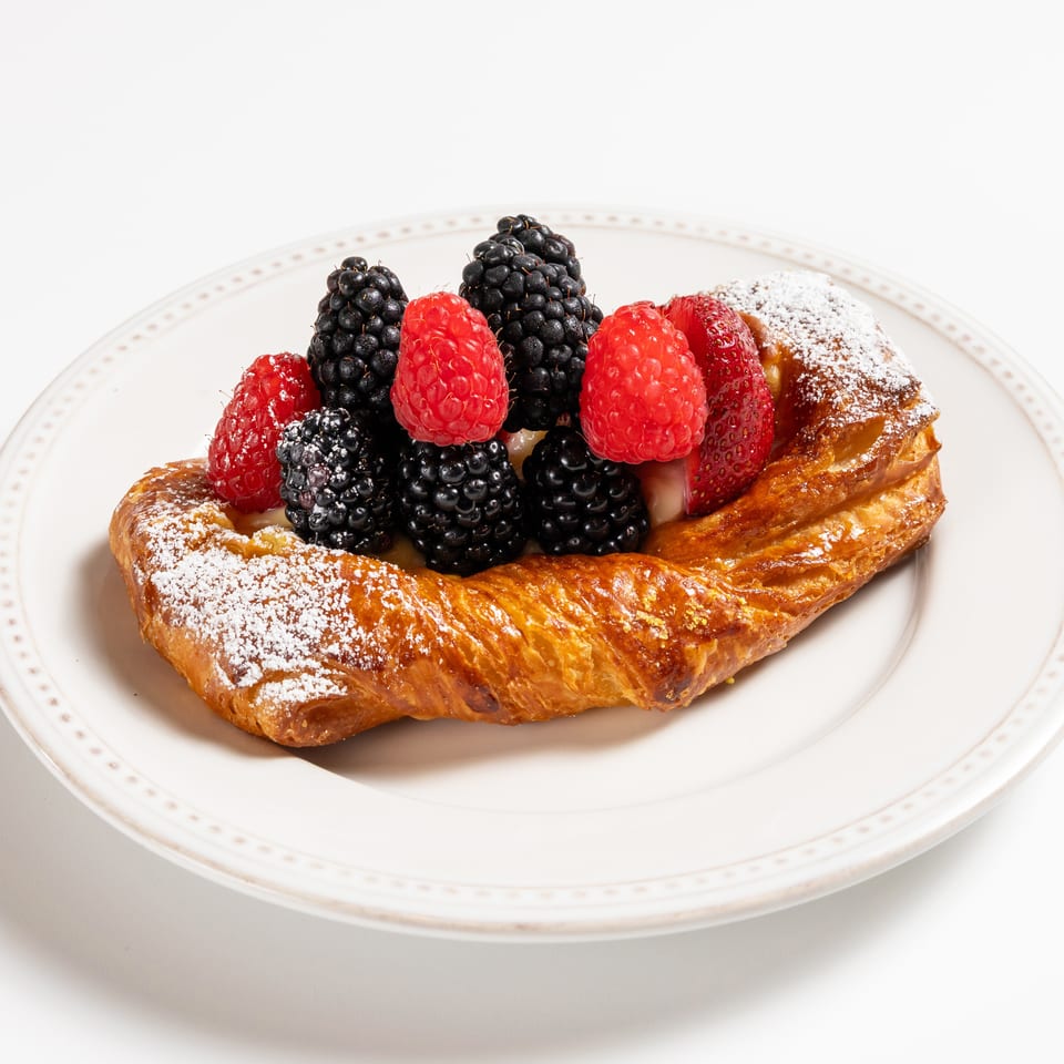 Golden pastry topped with fresh raspberries, blackberries, and powdered sugar on a white plate.