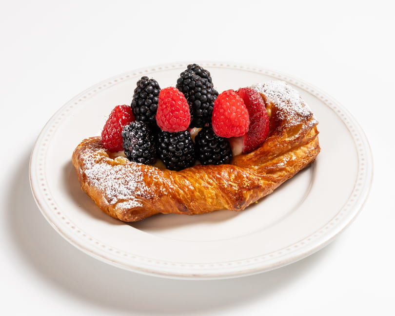 Golden pastry topped with fresh raspberries, blackberries, and powdered sugar on a white plate.