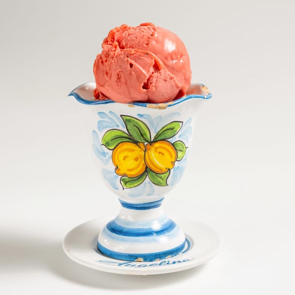 Scoop of strawberry ice cream in a decorative white, blue, and yellow ceramic cup.