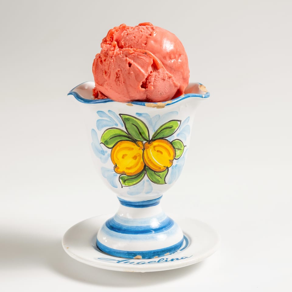 Scoop of strawberry ice cream in a decorative white, blue, and yellow ceramic cup.