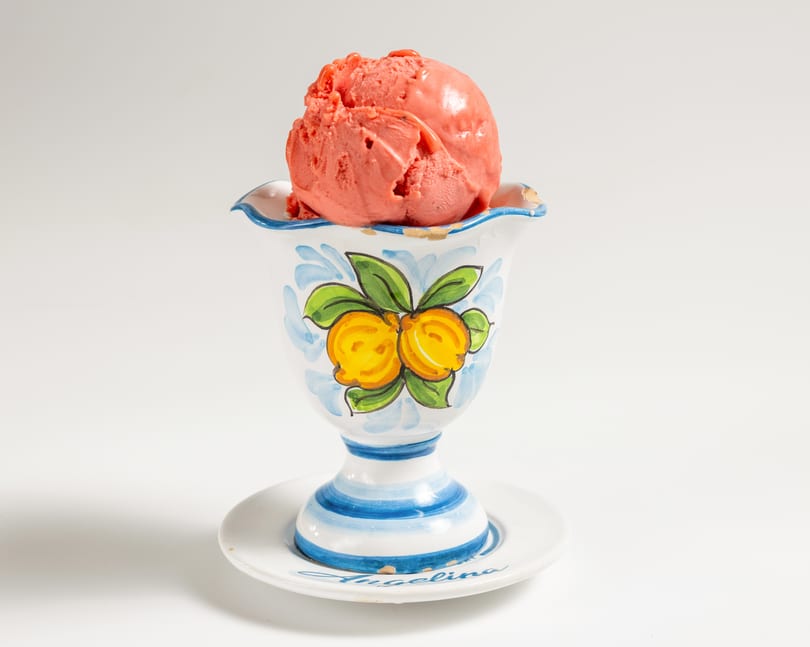 Scoop of strawberry ice cream in a decorative white, blue, and yellow ceramic cup.