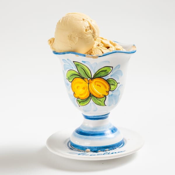 Scoops of light brown ice cream in a decorative white, blue, and yellow cup with a saucer.