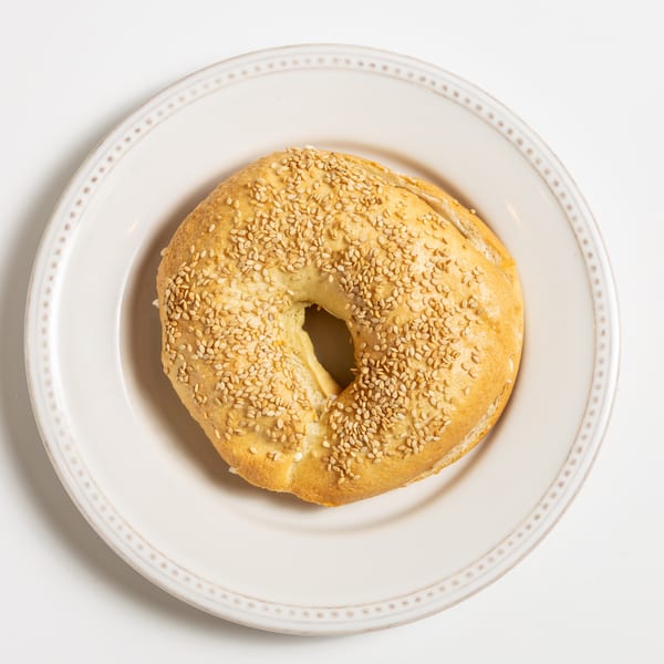 A sesame seed bagel with cream cheese on a white plate, viewed from directly above.