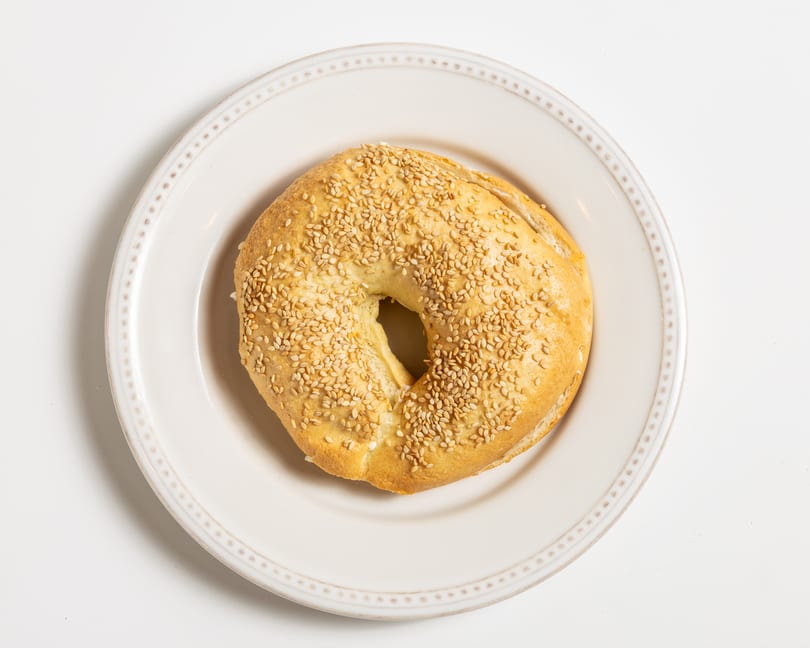A sesame seed bagel with cream cheese on a white plate, viewed from directly above.
